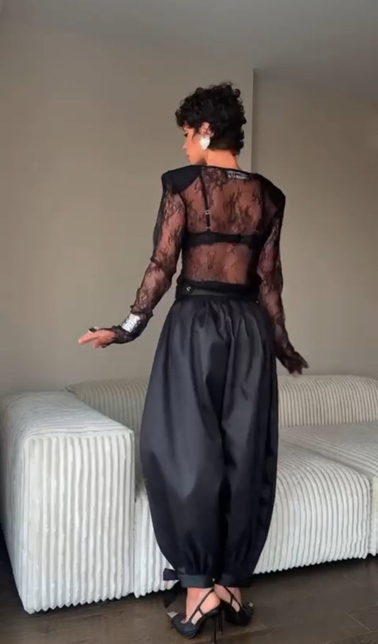 Outfit Ginevra elegante e sensuale composto da maglia in pizzo trasparente e pantalone nero a vita alta. Il pantalone presenta una linea fluida con spacco laterale e dettagli con fiocchi alla caviglia,